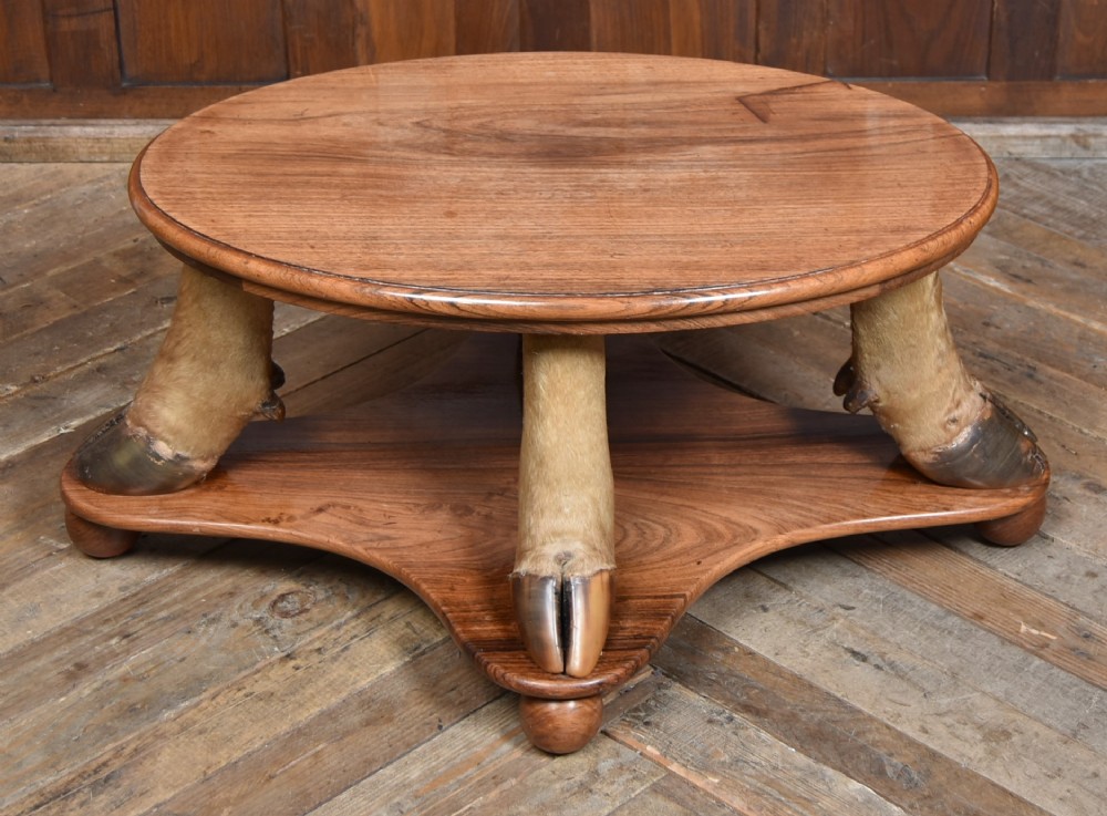 An oval polished wooden coffee table supported by four taxidermy hooves standing on a shaped wooden base with ball feet. View IX
