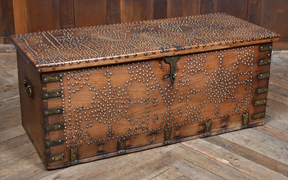 A solid padouk wood rectangular blanket box featuring intricate geometric brass stud patterns and metal strap reinforcements.