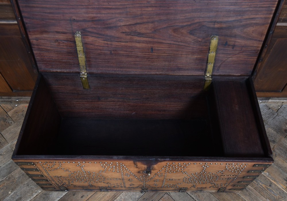 A solid padouk wood rectangular blanket box featuring intricate geometric brass stud patterns and metal strap reinforcements. View IX
