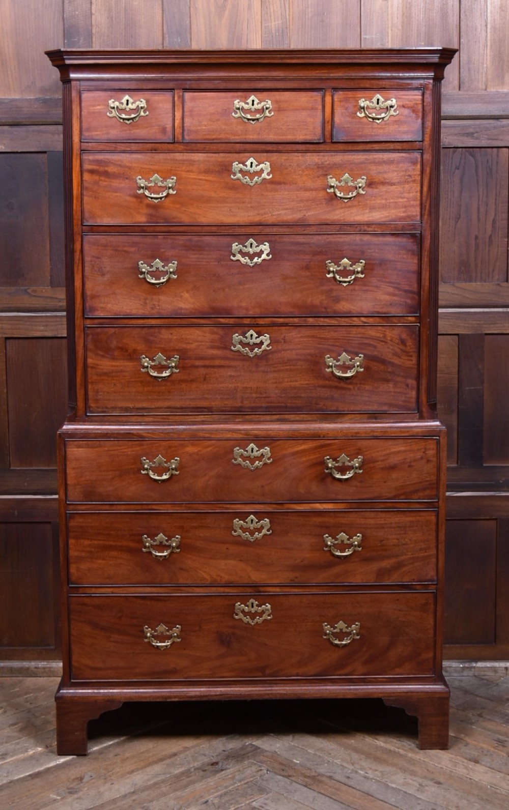 A tall Georgian mahogany chest on chest featuring two stacked tiers of drawers with brass swan-neck handles resting on bracket feet.