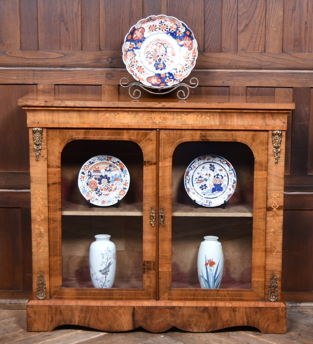A Victorian walnut pier cabinet featuring double glazed arched doors, floral marquetry inlay, and decorative ormolu mounts.