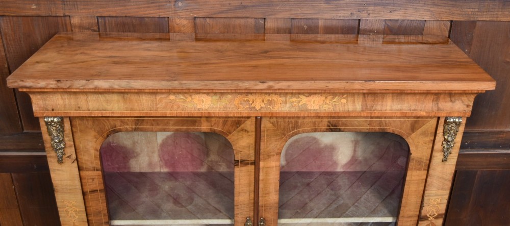 A Victorian walnut pier cabinet featuring double glazed arched doors, floral marquetry inlay, and decorative ormolu mounts. View IX