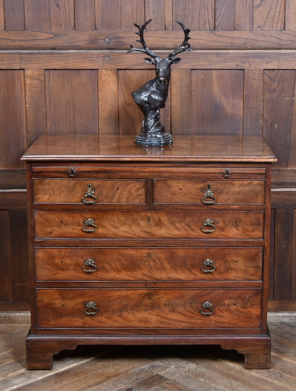 An 18th-century Georgian mahogany chest of drawers with a pull-out brushing slide, two short over three long graduated drawers, brass bail handles, and bracket feet.