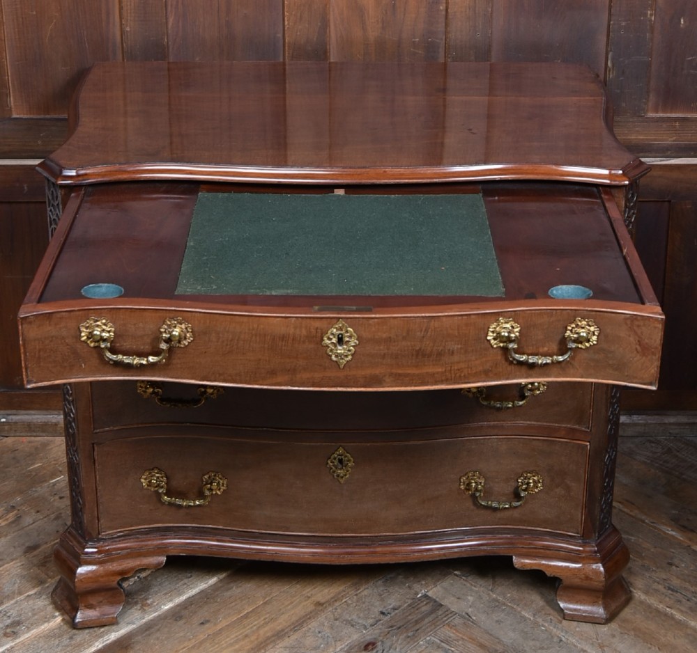 A Georgian mahogany chest of drawers featuring a serpentine front, four graduated drawers with ornate brass handles, and carved canted corners. View II