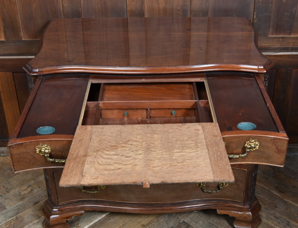 A Georgian mahogany chest of drawers featuring a serpentine front, four graduated drawers with ornate brass handles, and carved canted corners. View III