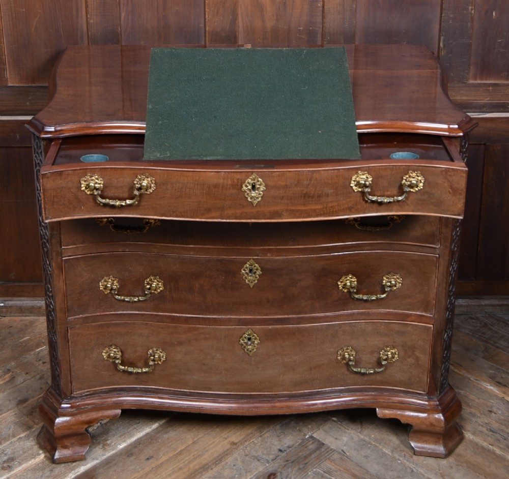 A Georgian mahogany chest of drawers featuring a serpentine front, four graduated drawers with ornate brass handles, and carved canted corners. View IV