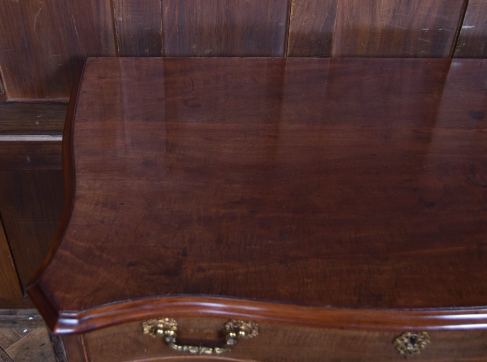 A Georgian mahogany chest of drawers featuring a serpentine front, four graduated drawers with ornate brass handles, and carved canted corners. View VIII