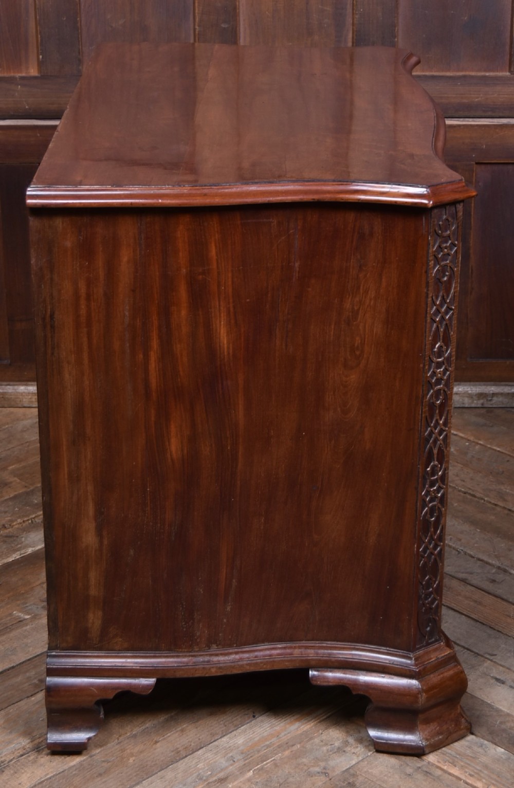 A Georgian mahogany chest of drawers featuring a serpentine front, four graduated drawers with ornate brass handles, and carved canted corners. View IX