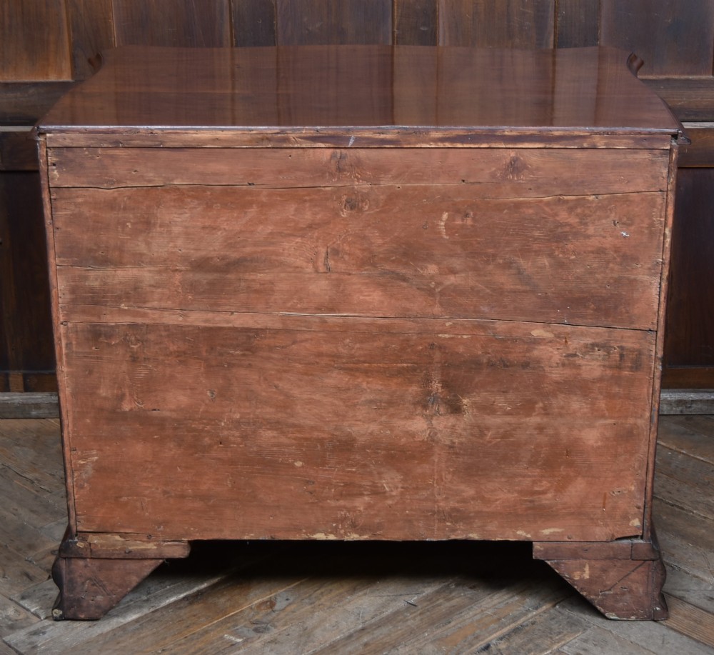 A Georgian mahogany chest of drawers featuring a serpentine front, four graduated drawers with ornate brass handles, and carved canted corners. View X