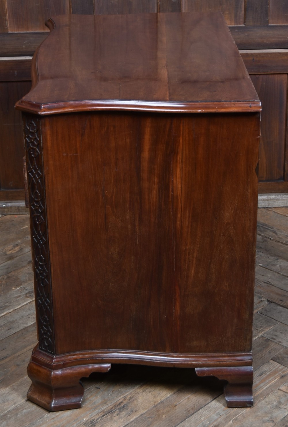 A Georgian mahogany chest of drawers featuring a serpentine front, four graduated drawers with ornate brass handles, and carved canted corners. View XI