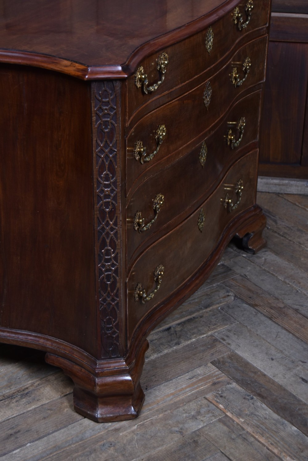 A Georgian mahogany chest of drawers featuring a serpentine front, four graduated drawers with ornate brass handles, and carved canted corners. View XII