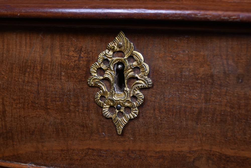 A Georgian mahogany chest of drawers featuring a serpentine front, four graduated drawers with ornate brass handles, and carved canted corners. View XV
