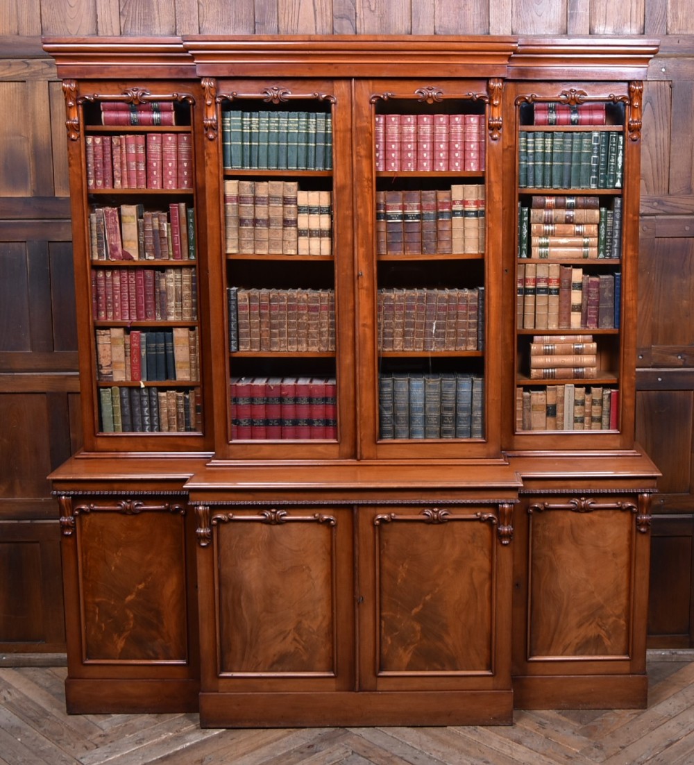 A large Victorian mahogany breakfront bookcase featuring four glazed upper doors and four panelled lower cupboard doors with carved details.