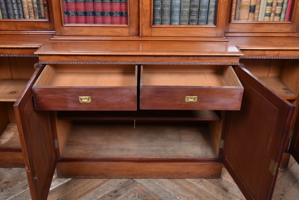 A large Victorian mahogany breakfront bookcase featuring four glazed upper doors and four panelled lower cupboard doors with carved details. View VI