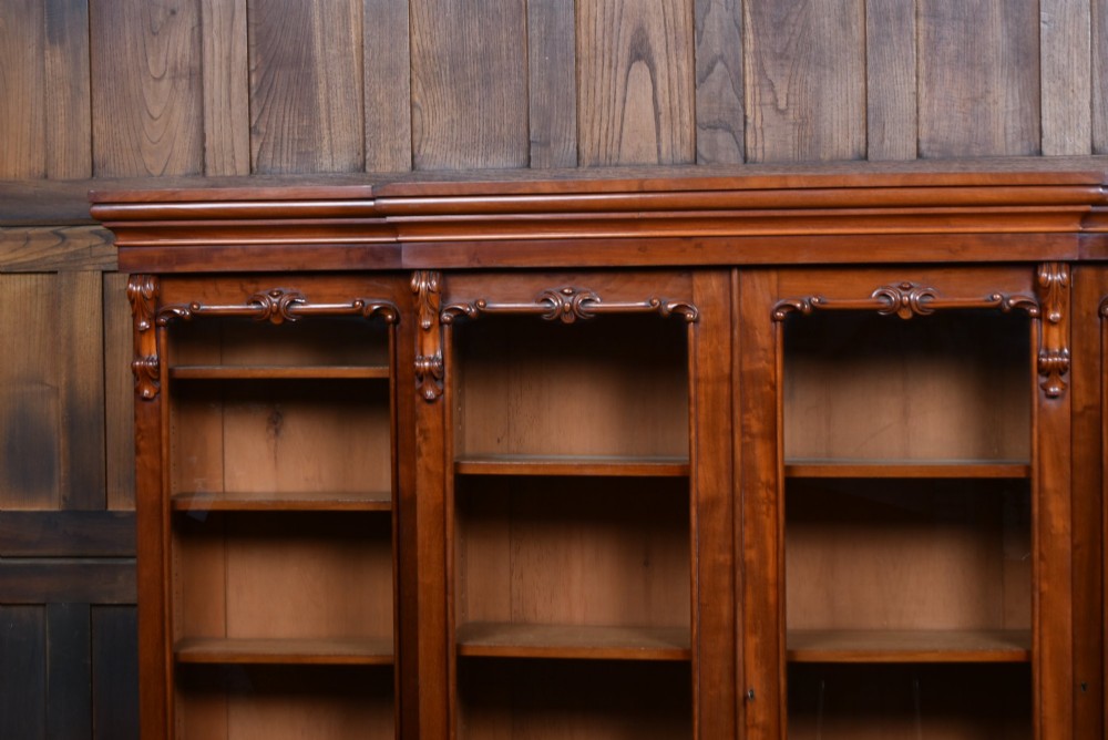 A large Victorian mahogany breakfront bookcase featuring four glazed upper doors and four panelled lower cupboard doors with carved details. View X