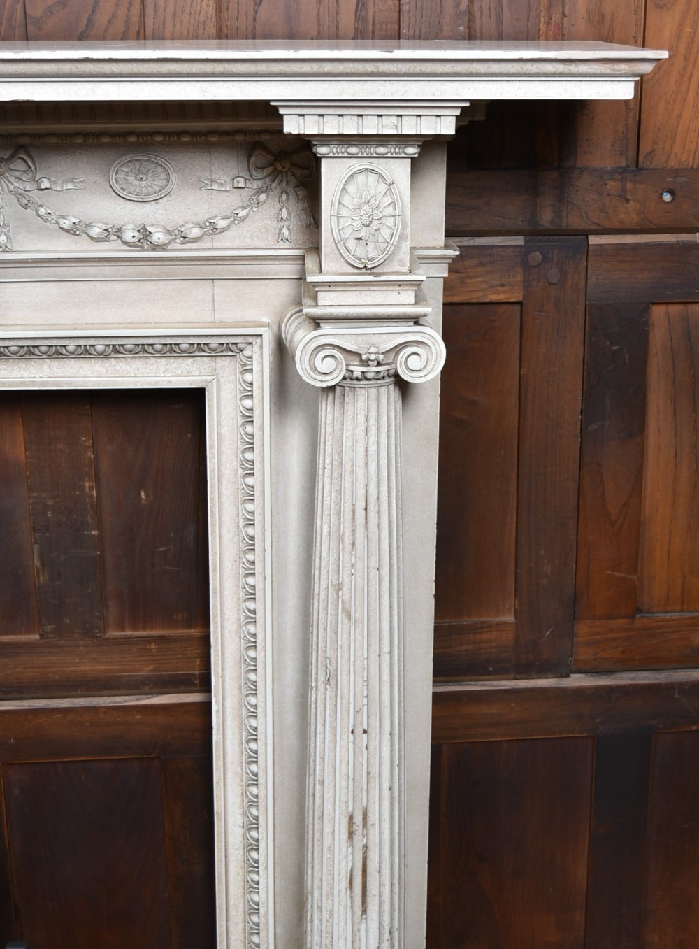An off-white painted Neoclassical fireplace surround featuring fluted columns and swags, paired with a black cast iron fire grate. View IV