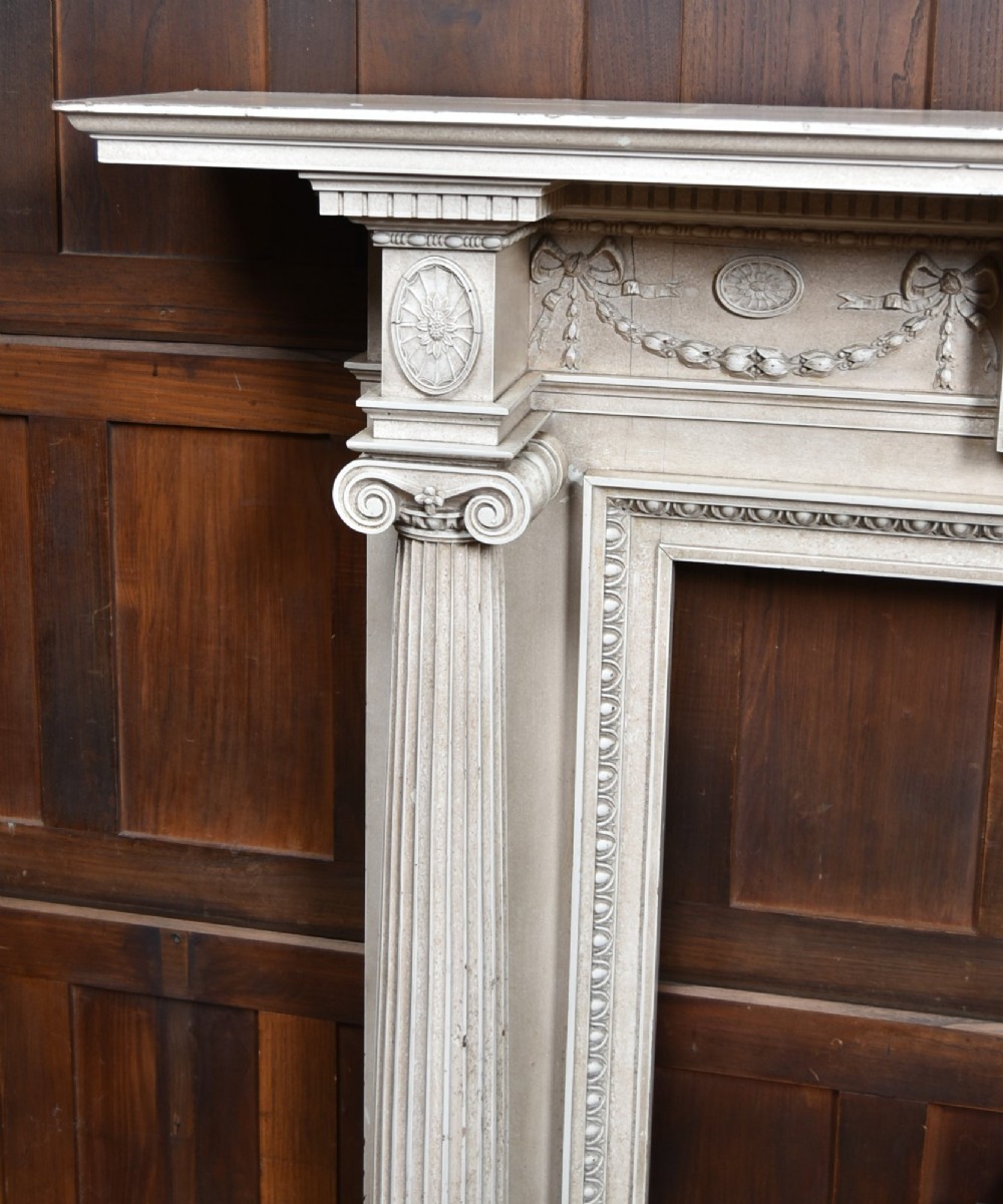 An off-white painted Neoclassical fireplace surround featuring fluted columns and swags, paired with a black cast iron fire grate. View V