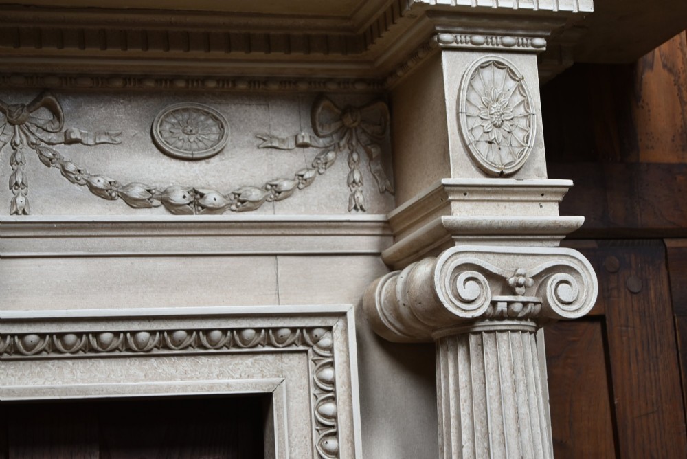 An off-white painted Neoclassical fireplace surround featuring fluted columns and swags, paired with a black cast iron fire grate. View X