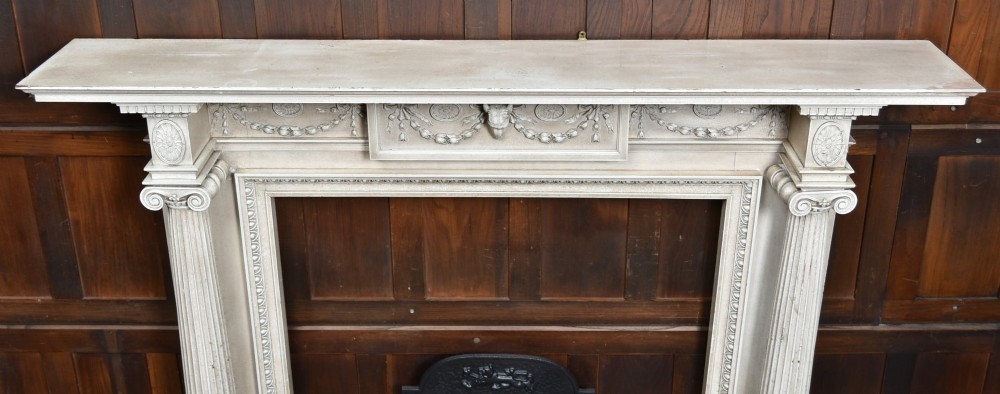 An off-white painted Neoclassical fireplace surround featuring fluted columns and swags, paired with a black cast iron fire grate. View XII