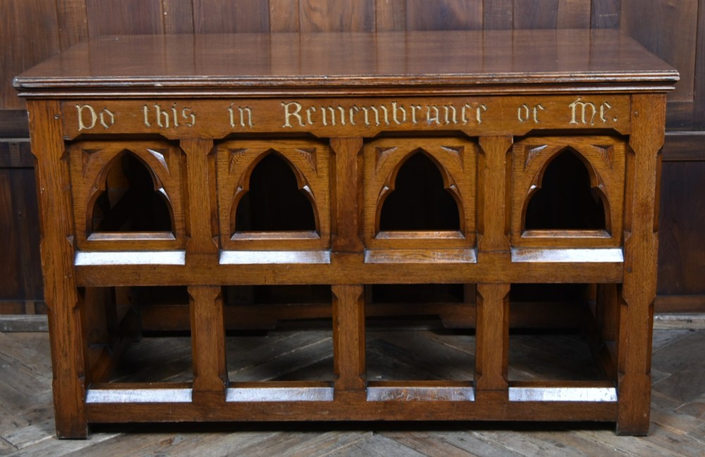A Victorian oak church communion table with carved Gothic arch panels and a carved inscription reading Do this in Remembrance of me along the top frieze.