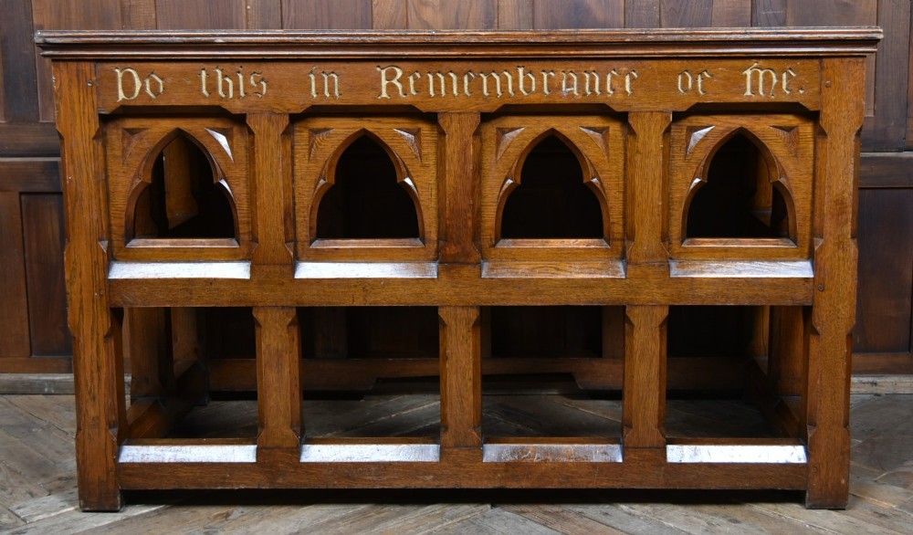 A Victorian oak church communion table with carved Gothic arch panels and a carved inscription reading Do this in Remembrance of me along the top frieze. View V
