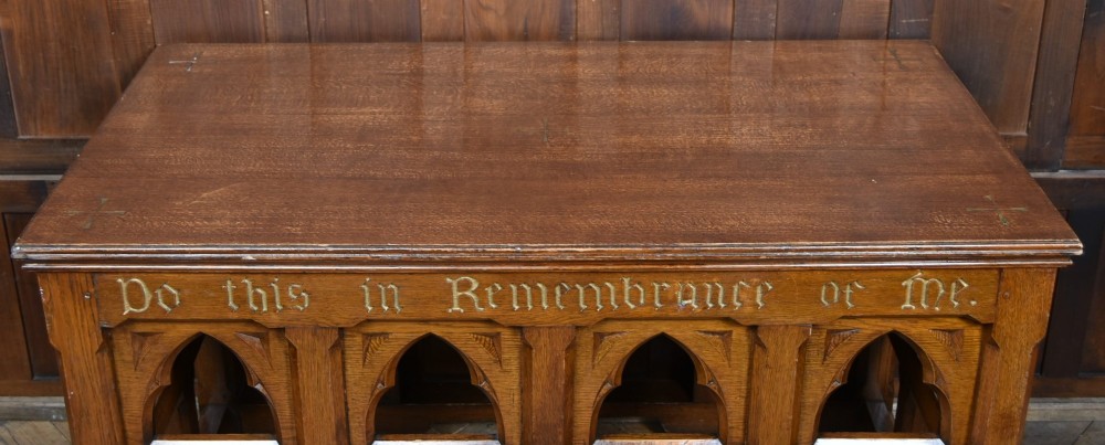 A Victorian oak church communion table with carved Gothic arch panels and a carved inscription reading Do this in Remembrance of me along the top frieze. View VI