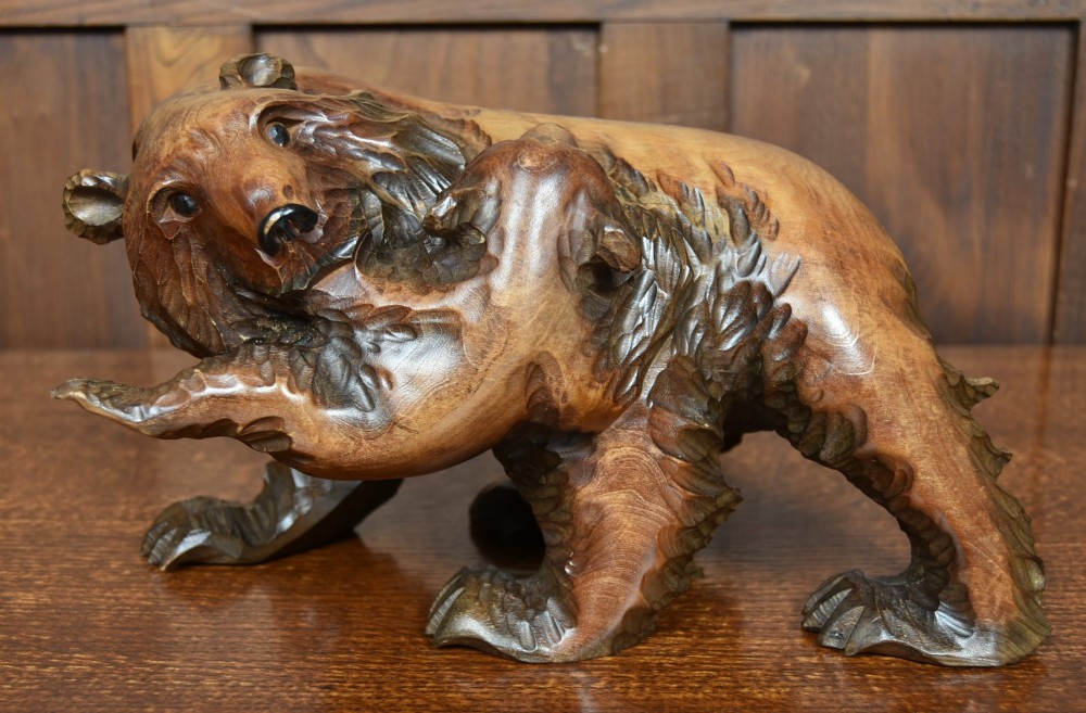 A hand-carved warm brown wooden sculpture depicting a mother bear with a cub clinging to her side. View II