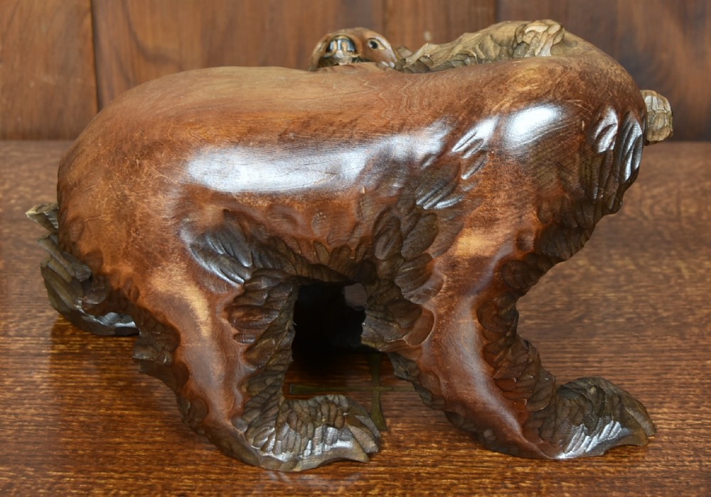 A hand-carved warm brown wooden sculpture depicting a mother bear with a cub clinging to her side. View V