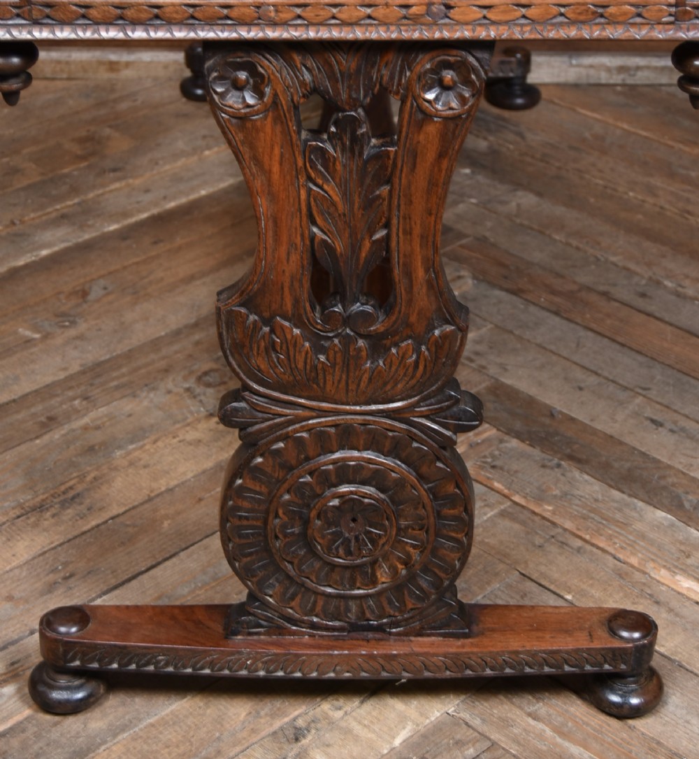 A dark brown padouk wood side table featuring a deeply carved floral gallery back, three carved drawer fronts, and trestle legs connected by a turned stretcher. View XV