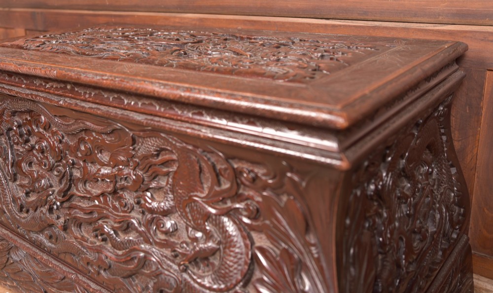 A dark brown rectangular carved hardwood storage chest decorated with high-relief dragon and cloud motifs on all visible faces. View IV