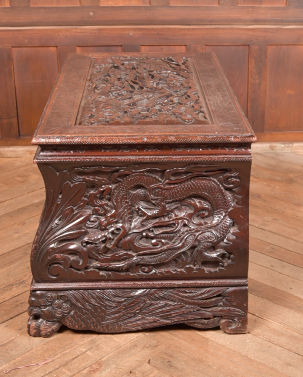 A dark brown rectangular carved hardwood storage chest decorated with high-relief dragon and cloud motifs on all visible faces. View VIII