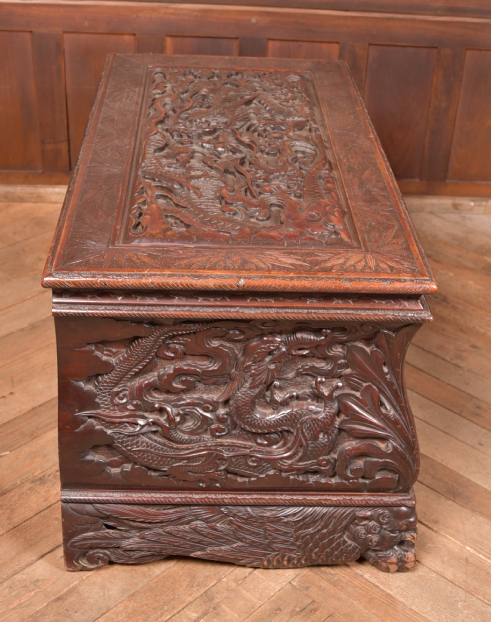 A dark brown rectangular carved hardwood storage chest decorated with high-relief dragon and cloud motifs on all visible faces. View XI