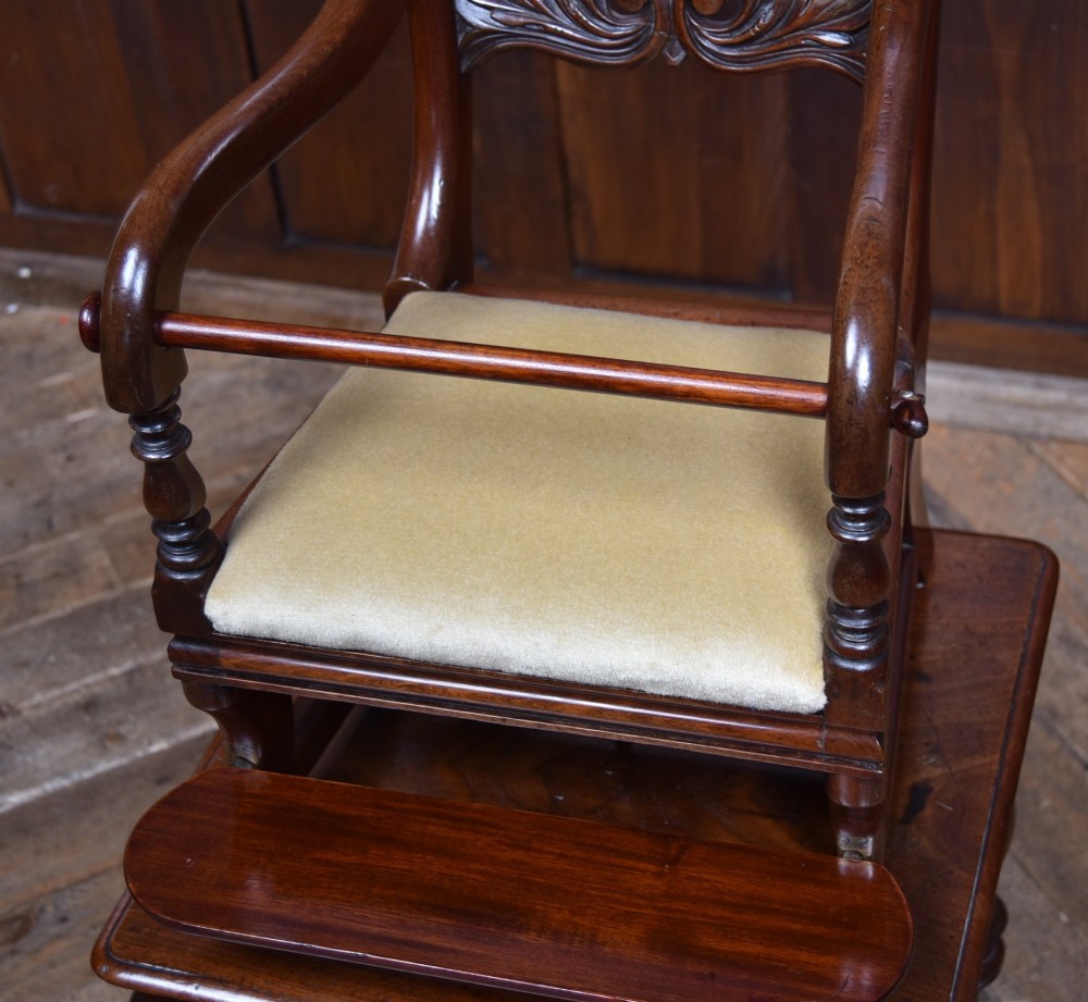A Victorian metamorphic mahogany childs high chair with turned legs, curved armrests, a carved backrest crest, and cream fabric upholstery. View IV