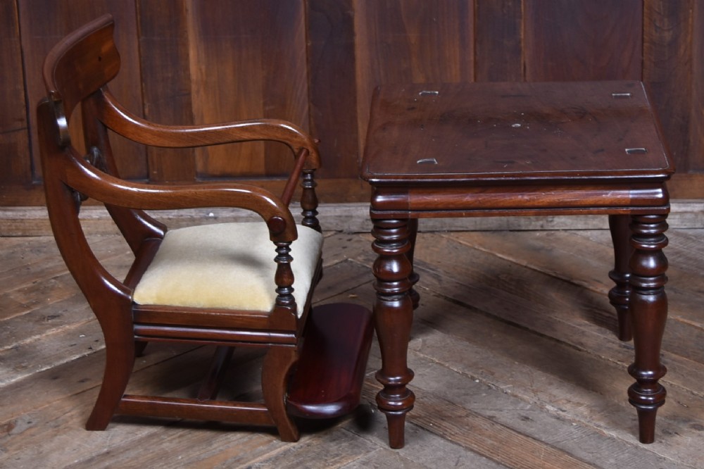 A Victorian metamorphic mahogany childs high chair with turned legs, curved armrests, a carved backrest crest, and cream fabric upholstery. View X