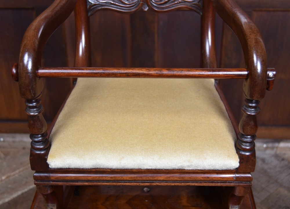 A Victorian metamorphic mahogany childs high chair with turned legs, curved armrests, a carved backrest crest, and cream fabric upholstery. View XIII