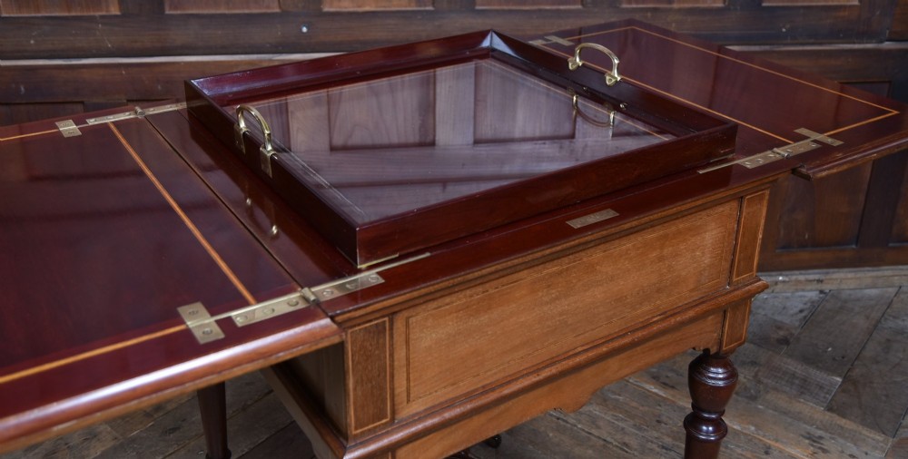 An Edwardian mahogany drinks cabinet table featuring hinged folding top leaves, a rising central tray mechanism, satinwood inlay, and turned legs on brass castors. View III