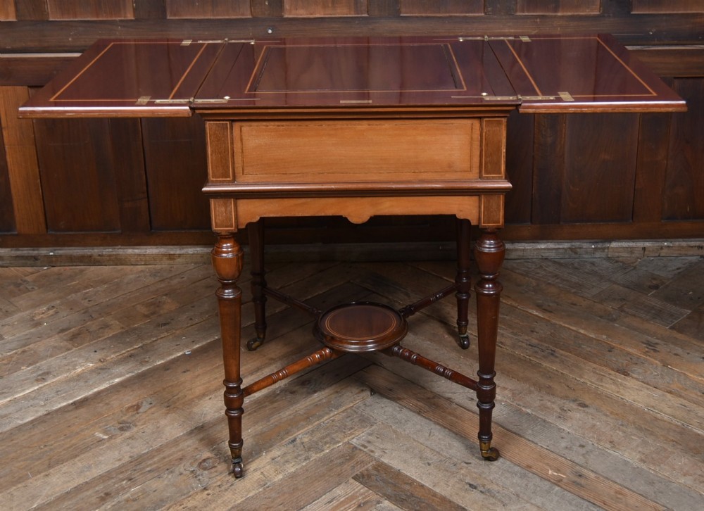 An Edwardian mahogany drinks cabinet table featuring hinged folding top leaves, a rising central tray mechanism, satinwood inlay, and turned legs on brass castors. View VII