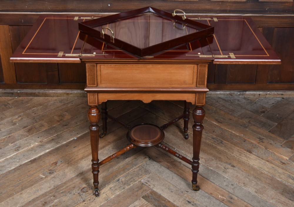An Edwardian mahogany drinks cabinet table featuring hinged folding top leaves, a rising central tray mechanism, satinwood inlay, and turned legs on brass castors. View VIII