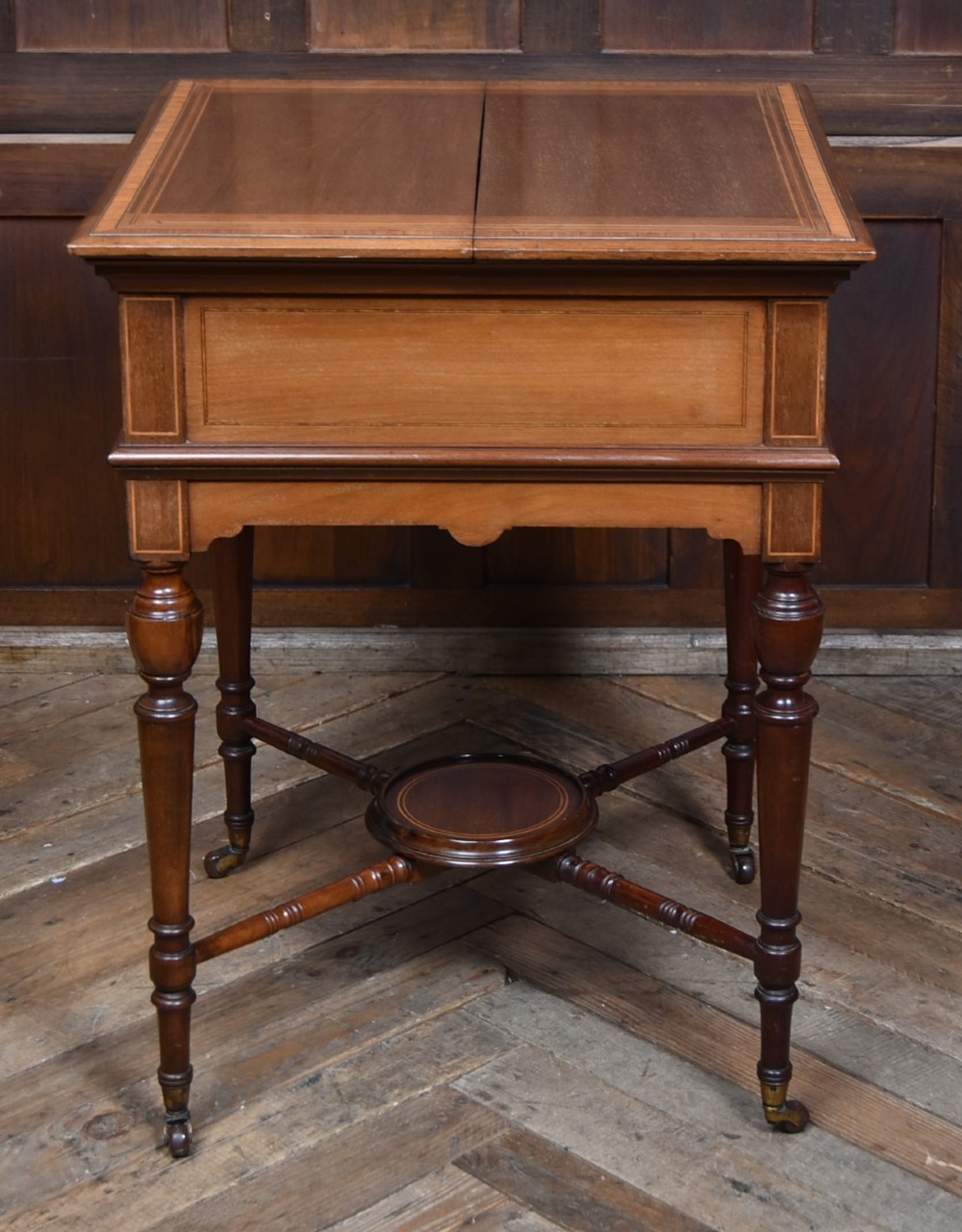 An Edwardian mahogany drinks cabinet table featuring hinged folding top leaves, a rising central tray mechanism, satinwood inlay, and turned legs on brass castors. View XI
