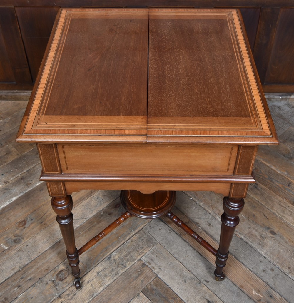 An Edwardian mahogany drinks cabinet table featuring hinged folding top leaves, a rising central tray mechanism, satinwood inlay, and turned legs on brass castors. View XII