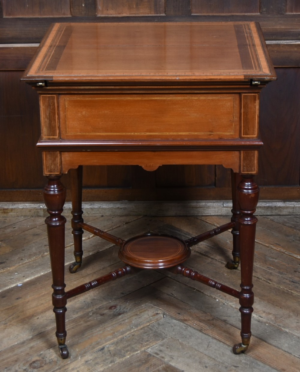 An Edwardian mahogany drinks cabinet table featuring hinged folding top leaves, a rising central tray mechanism, satinwood inlay, and turned legs on brass castors. View XIV