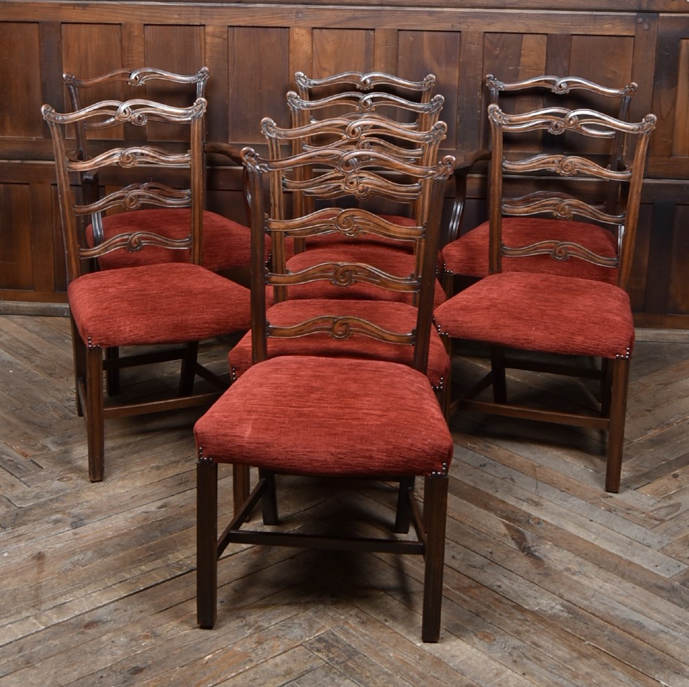 A set of Chippendale Revival mahogany dining chairs featuring carved ladder-back splats and red upholstered seats.
