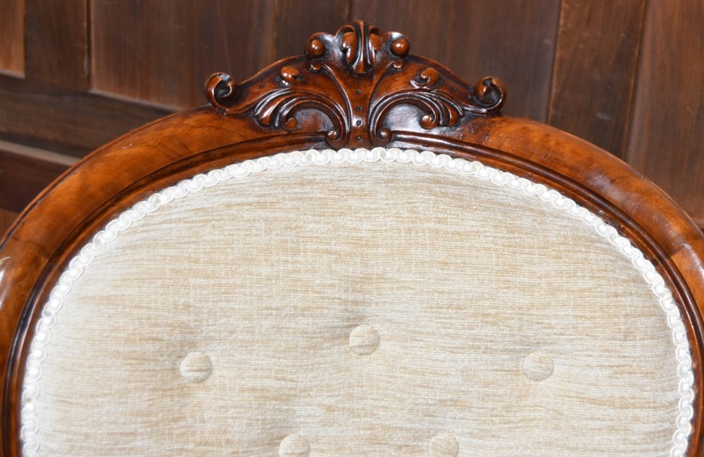 A Victorian walnut spoon-back armchair upholstered in neutral fabric with button tufting, carved scroll arms, cabriole legs, and castors. View II