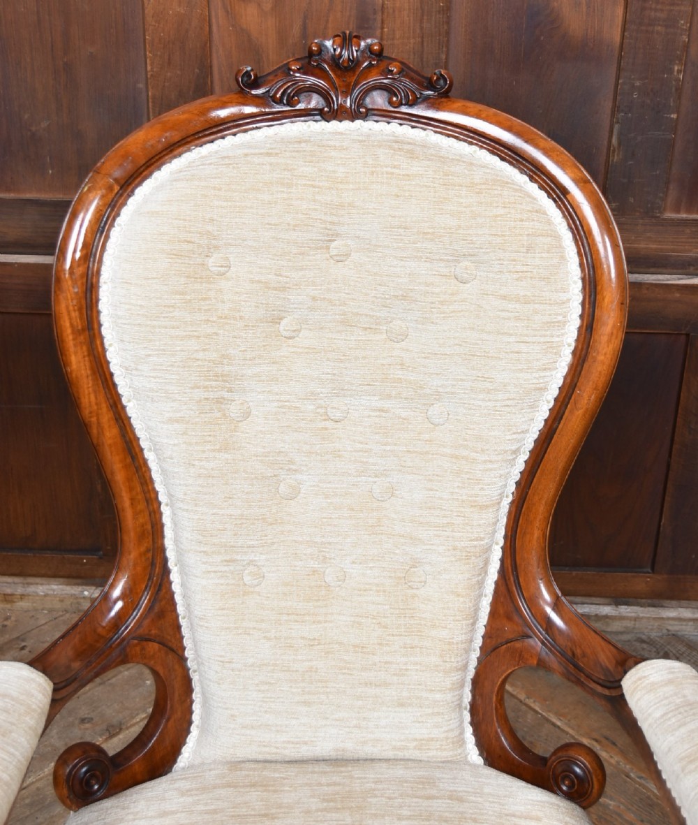 A Victorian walnut spoon-back armchair upholstered in neutral fabric with button tufting, carved scroll arms, cabriole legs, and castors. View III