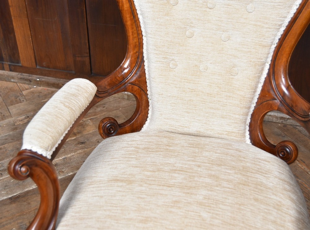 A Victorian walnut spoon-back armchair upholstered in neutral fabric with button tufting, carved scroll arms, cabriole legs, and castors. View IV