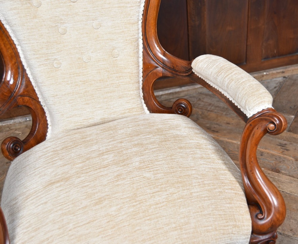 A Victorian walnut spoon-back armchair upholstered in neutral fabric with button tufting, carved scroll arms, cabriole legs, and castors. View V