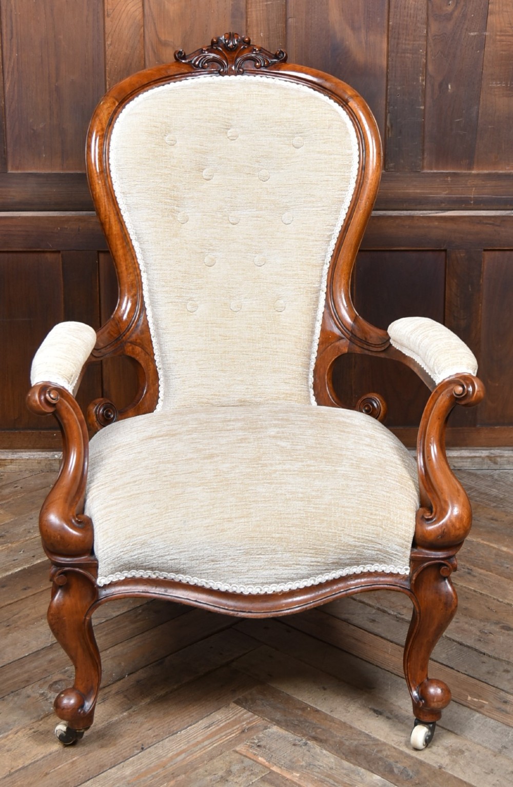 A Victorian walnut spoon-back armchair upholstered in neutral fabric with button tufting, carved scroll arms, cabriole legs, and castors. View VII
