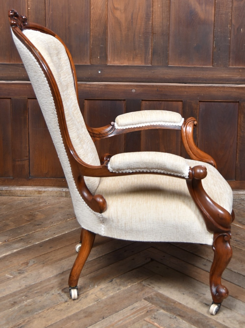 A Victorian walnut spoon-back armchair upholstered in neutral fabric with button tufting, carved scroll arms, cabriole legs, and castors. View VIII