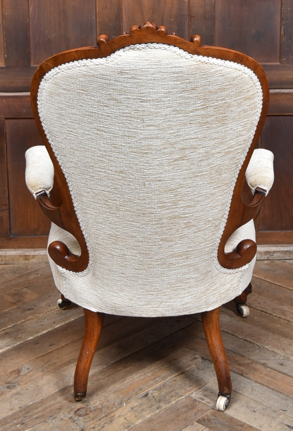 A Victorian walnut spoon-back armchair upholstered in neutral fabric with button tufting, carved scroll arms, cabriole legs, and castors. View IX