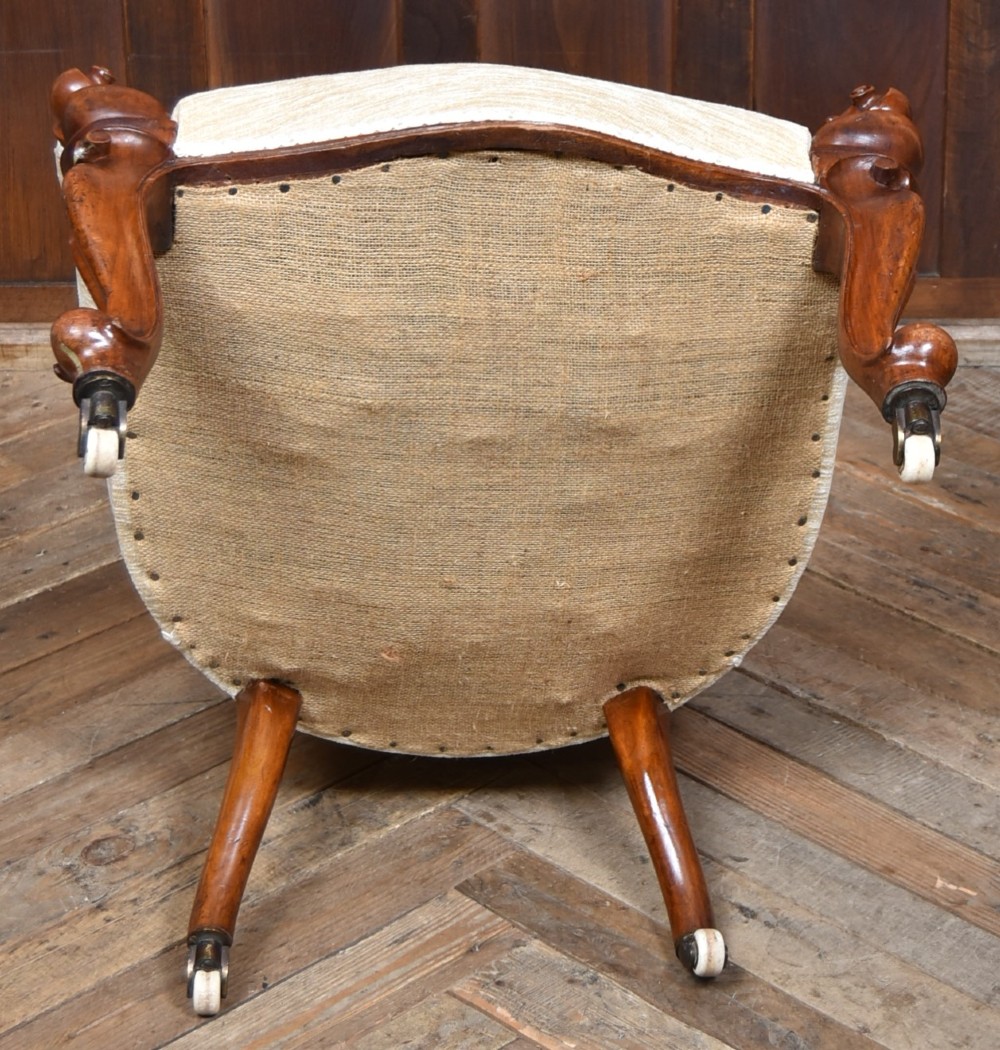 A Victorian walnut spoon-back armchair upholstered in neutral fabric with button tufting, carved scroll arms, cabriole legs, and castors. View XI